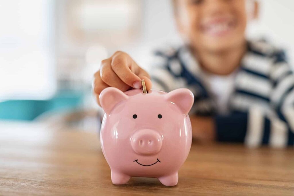 Kind wirft eine Münze in ein rosa Sparschwein