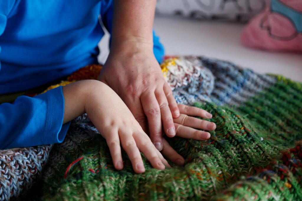 Hände einer Pflegeperson und eines Kindes auf einer grünen Strickdecke