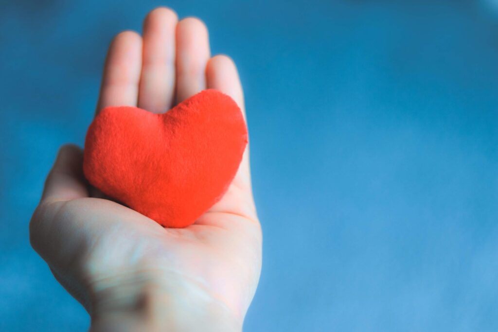 Hand hält ein rotes Herz vor blauem Hintergrund